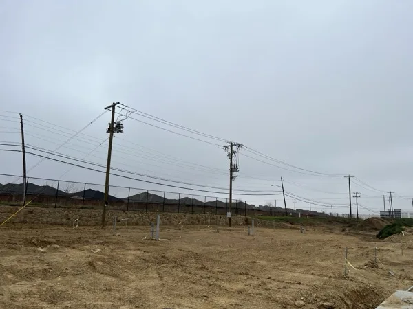 New utility poles with cutouts and a transformer bank along a graded site under an overcast sky