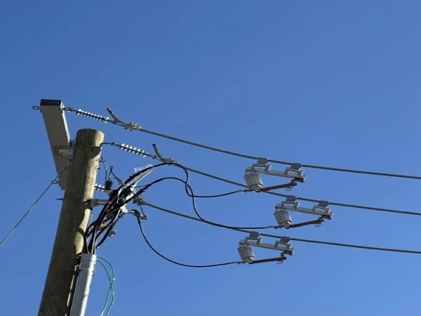 Pole top with three fused cutouts, arresters and riser cables against a blue sky