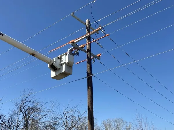 Lineman bucket at a crossarm with new jumpers and insulators against a blue sky