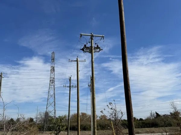 New wood pole set next to an existing distribution line with a transmission tower behind