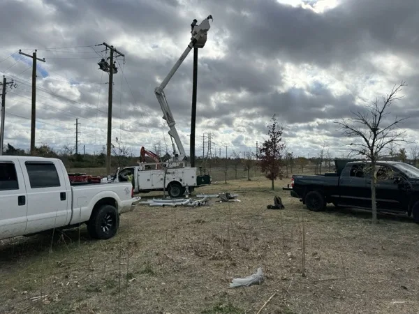 Line crew in a bucket truck setting a pole, with service trucks and conduit on the ground