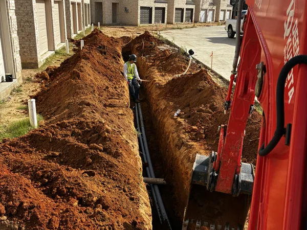 Mini excavator digging a trench along a row of townhomes