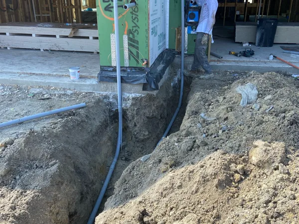 Conduits rising into a framed building from a trench, with a worker beside them