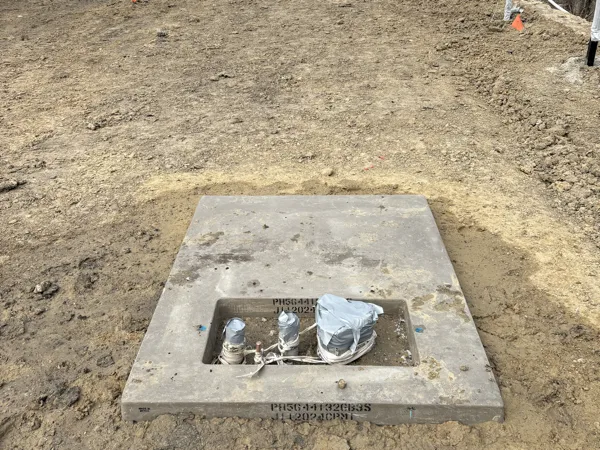 Concrete transformer pad set on the site with a cable reel behind