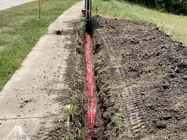 Trench with caution tape running along a street beside a sidewalk