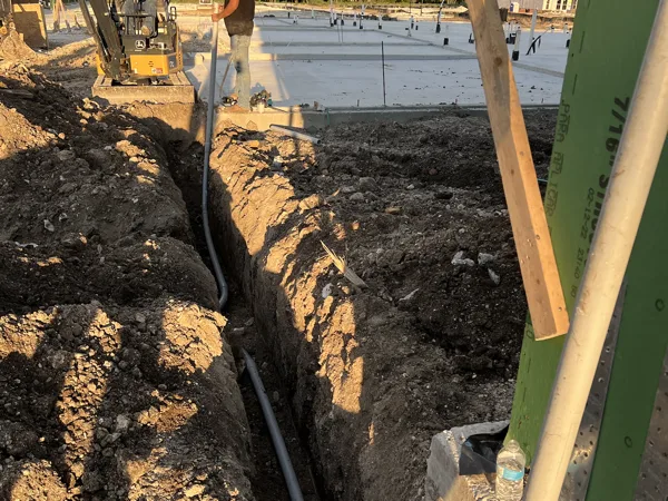 Conduit riser at the corner of a framed building with a trench leading to it