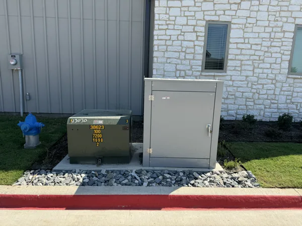 Pad mounted transformer and meter cabinet beside a finished stone building